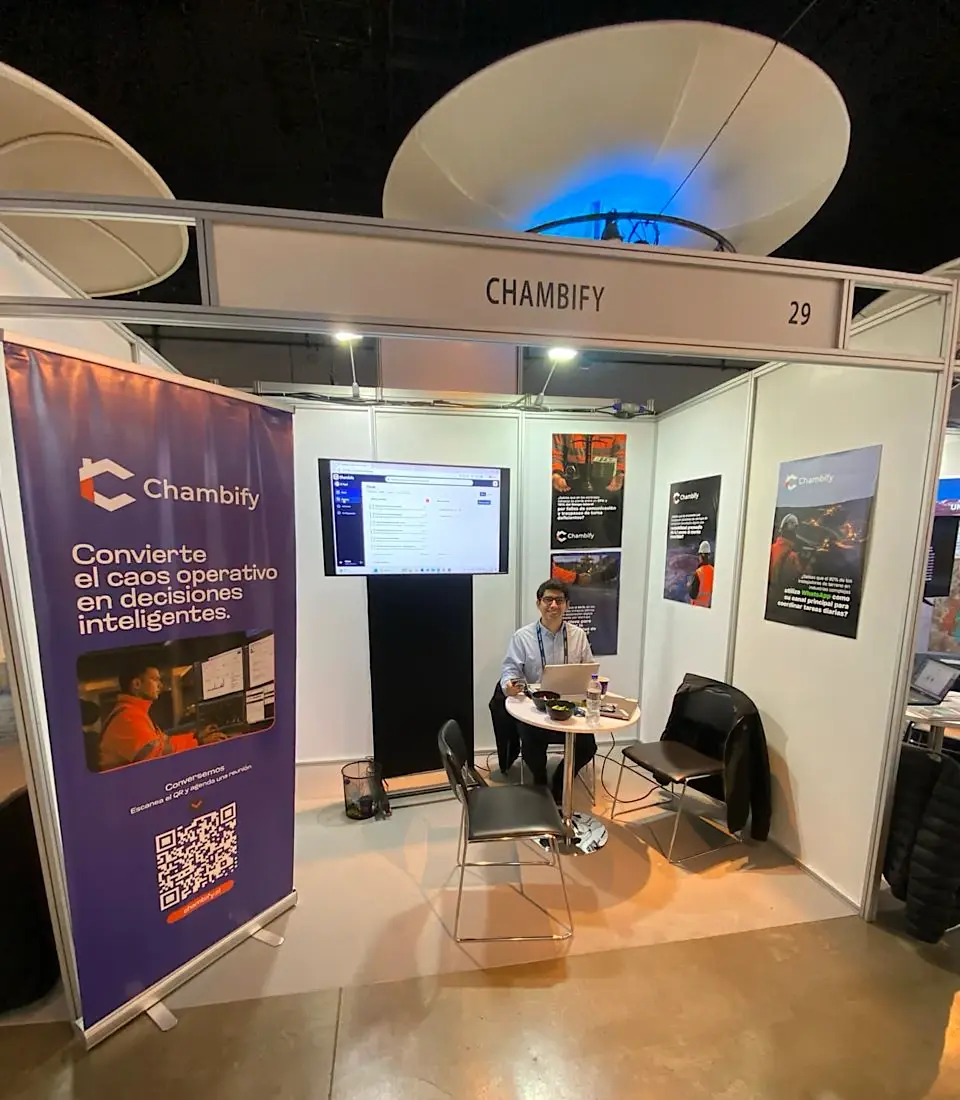 Stand 29 de Chambify en FEXMIN 2026: un integrante del equipo en la mesa, la plataforma en pantalla y el pendón de la marca